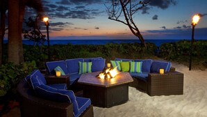 A beachside seating area with a fire pit, surrounded by lush greenery and overlooking the ocean. - Jupiter Beach Resort & Spa (Jupiter)