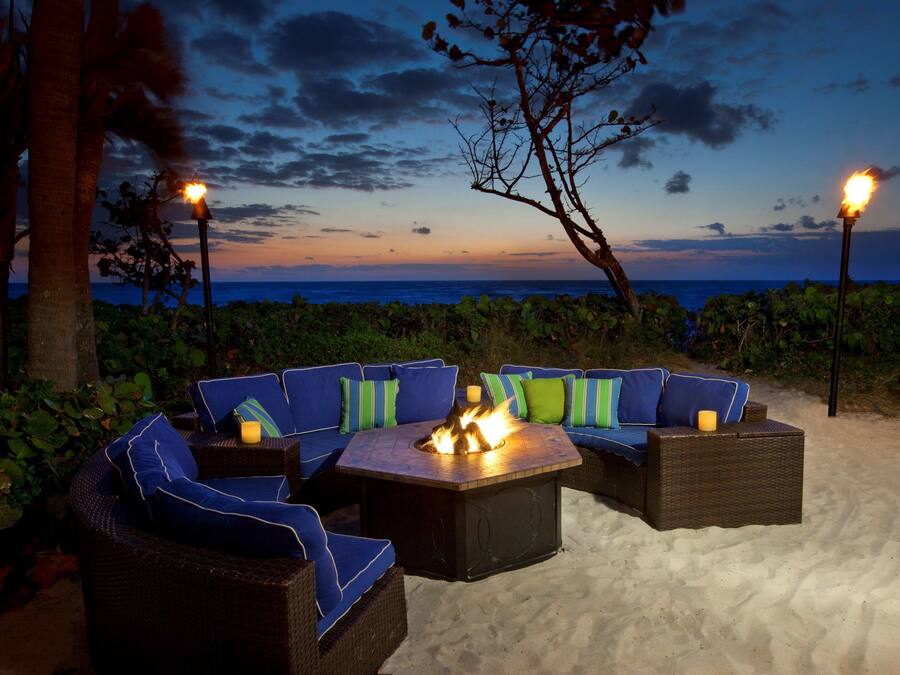 A beachside seating area with a fire pit, surrounded by lush greenery and overlooking the ocean.