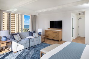 A modern hotel room with a large bed, a sofa, a TV, and a view of the ocean.