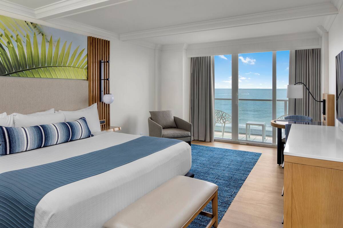 A hotel room with a large bed, a desk, a chair, and a view of the ocean.