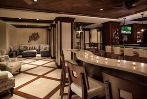A bar area with a curved counter, bar stools, and a television mounted above the bar.