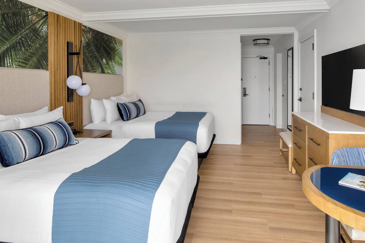 A hotel room with two beds, a wooden headboard, a desk, and a TV.
