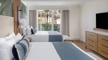A hotel room with two beds, a TV, a wooden dresser, and a large window with a view of palm trees and buildings.