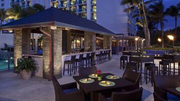 An outdoor bar area with seating and a pool in the background.
