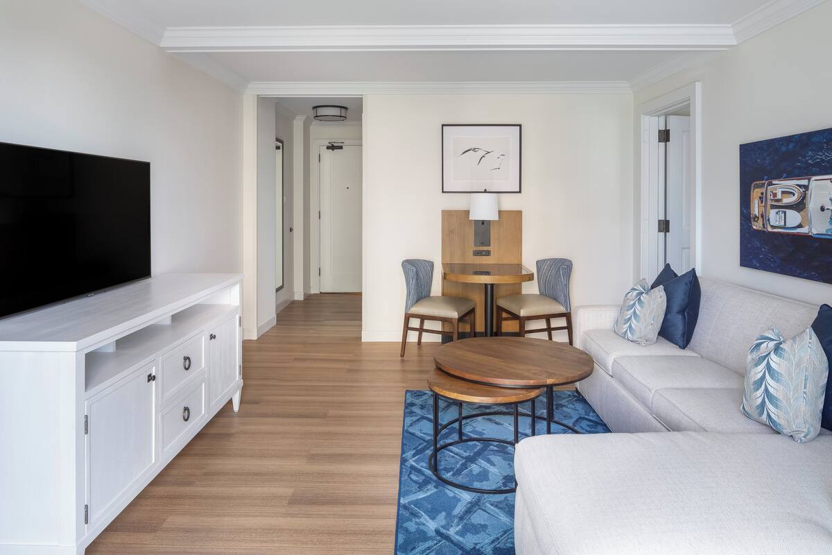 A modern living room with a flat-screen TV, a sofa, a coffee table, and a dining area with chairs and a table.