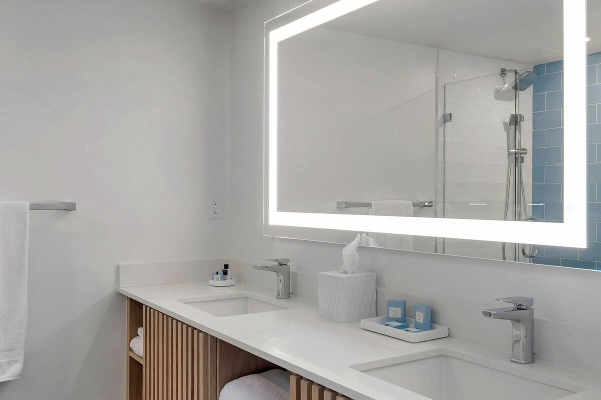 A modern bathroom with a large mirror, two sinks, and a wooden vanity.