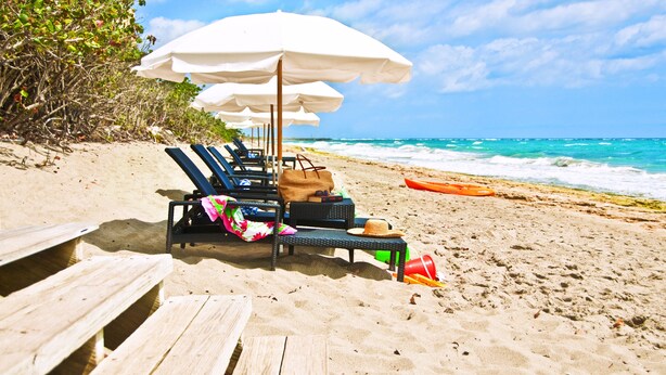 A beach with lounge chairs and umbrellas, a wooden deck, and a view of the ocean. - Jupiter Beach Resort & Spa (Jupiter)