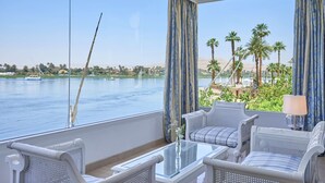 A balcony with wicker furniture, a glass table, and a view of a lake with palm trees and a boat.