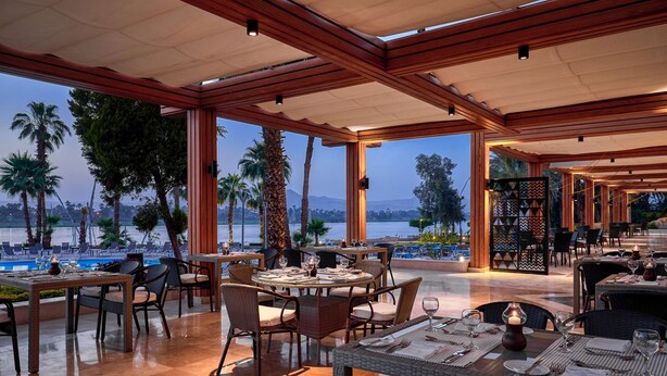 An outdoor dining area with tables and chairs, overlooking a pool and palm trees.