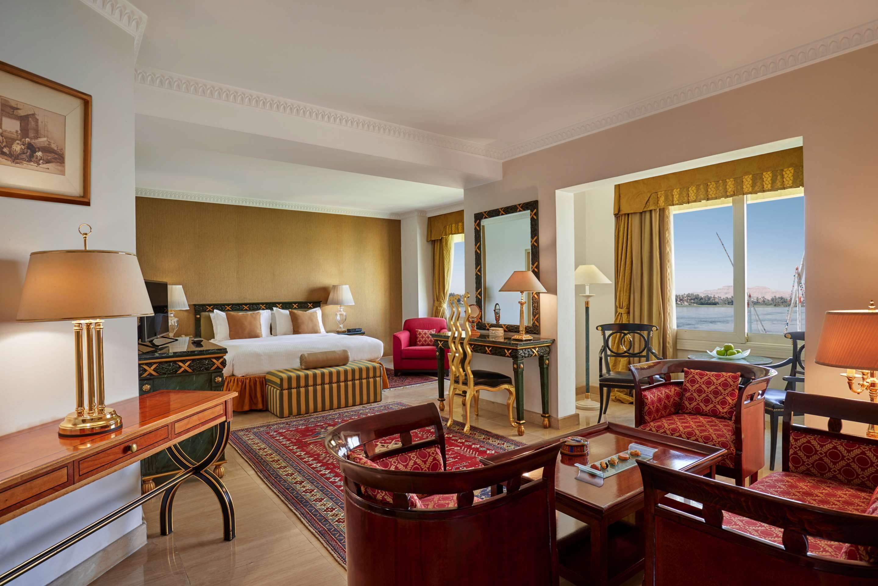 A hotel room with a bed, a desk, a dining area, and a view of the outdoors.