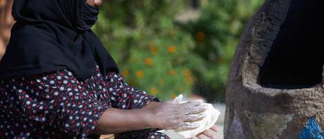 A person kneading dough on a flat surface with a traditional oven in the background.