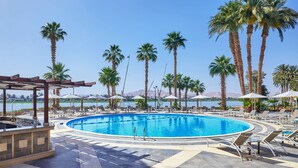 A pool area with lounge chairs, umbrellas, and palm trees.