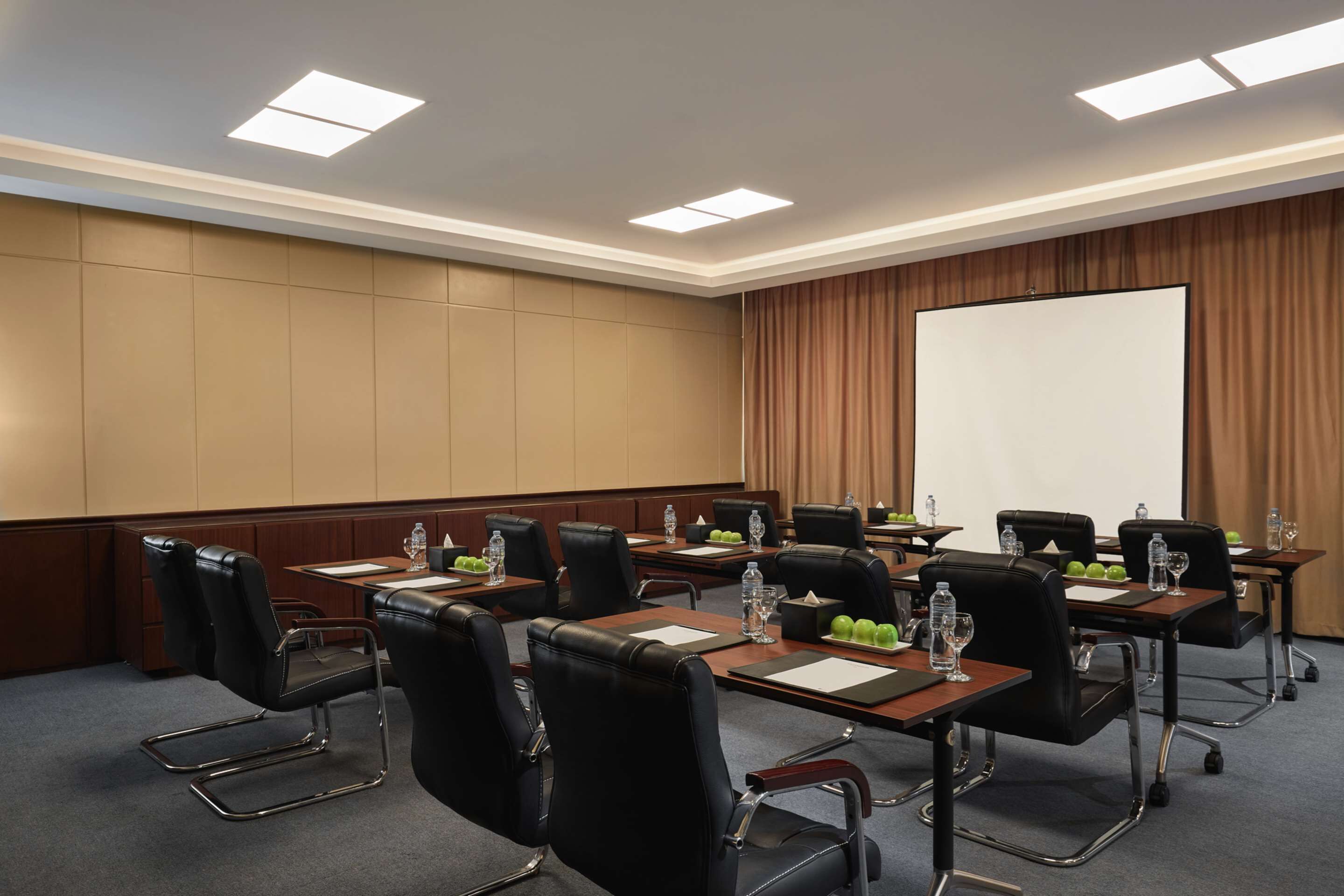 A conference room with multiple tables, chairs, and a large screen.