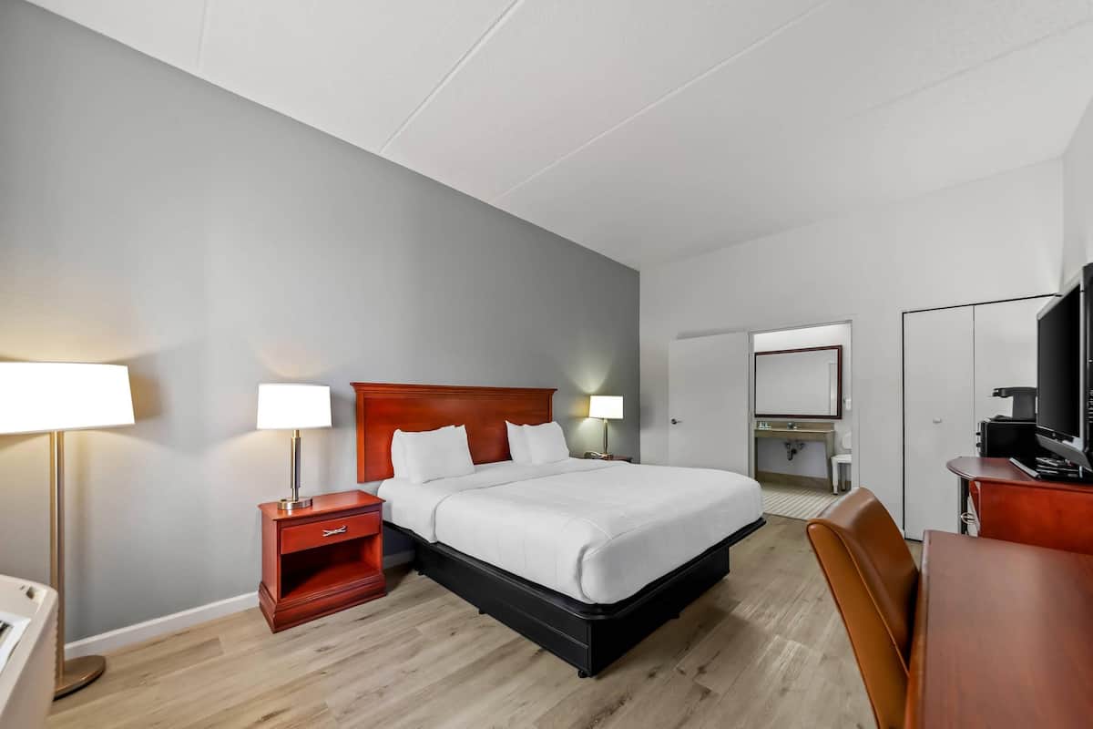 A hotel room with a bed, bedside tables, a desk, a chair, a TV, and a bathroom.