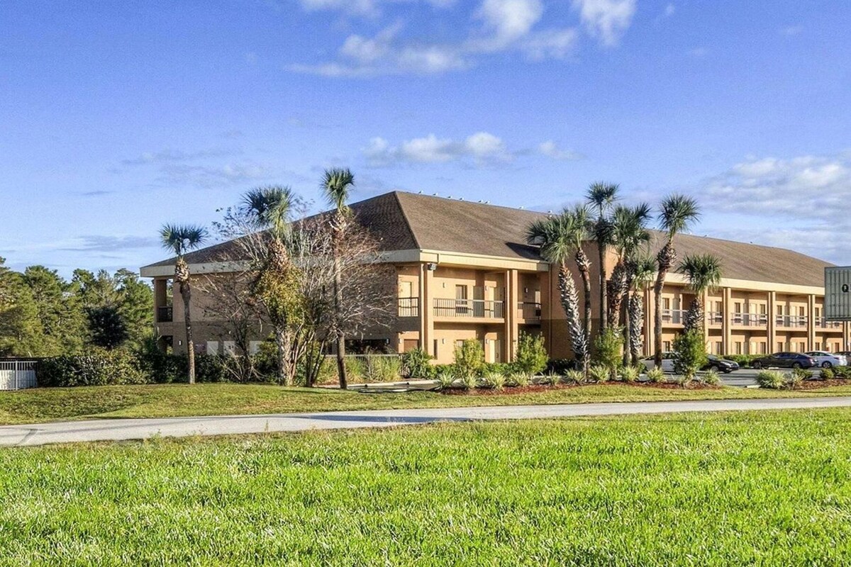 A multi-story hotel with a flat roof, surrounded by palm trees and a well-maintained lawn.