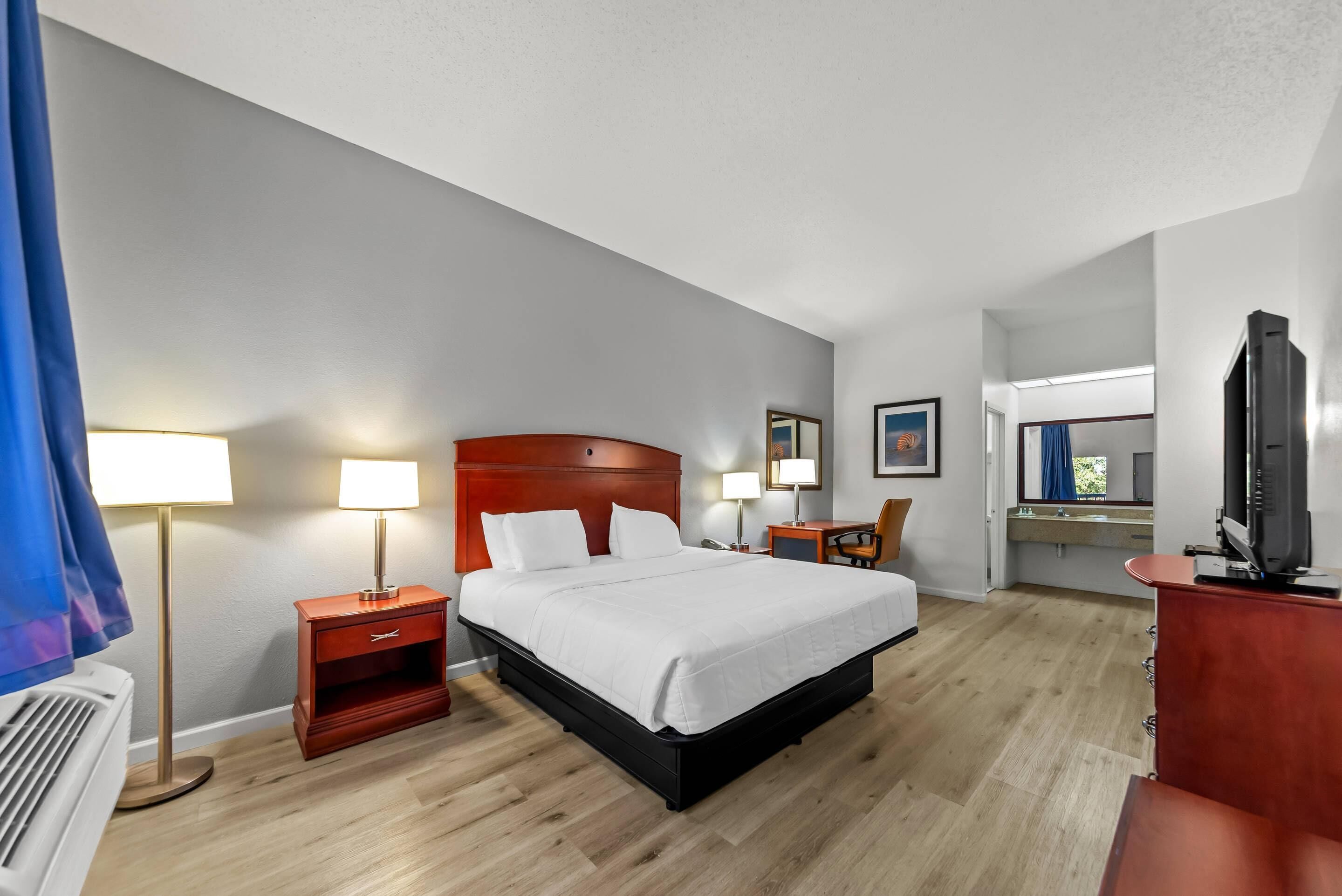 A hotel room with a large bed, bedside tables, a desk, and a television.