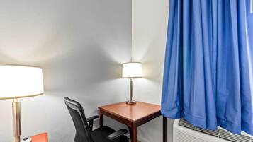 Habitación de hotel con escritorio, silla, lámpara y aire acondicionado.