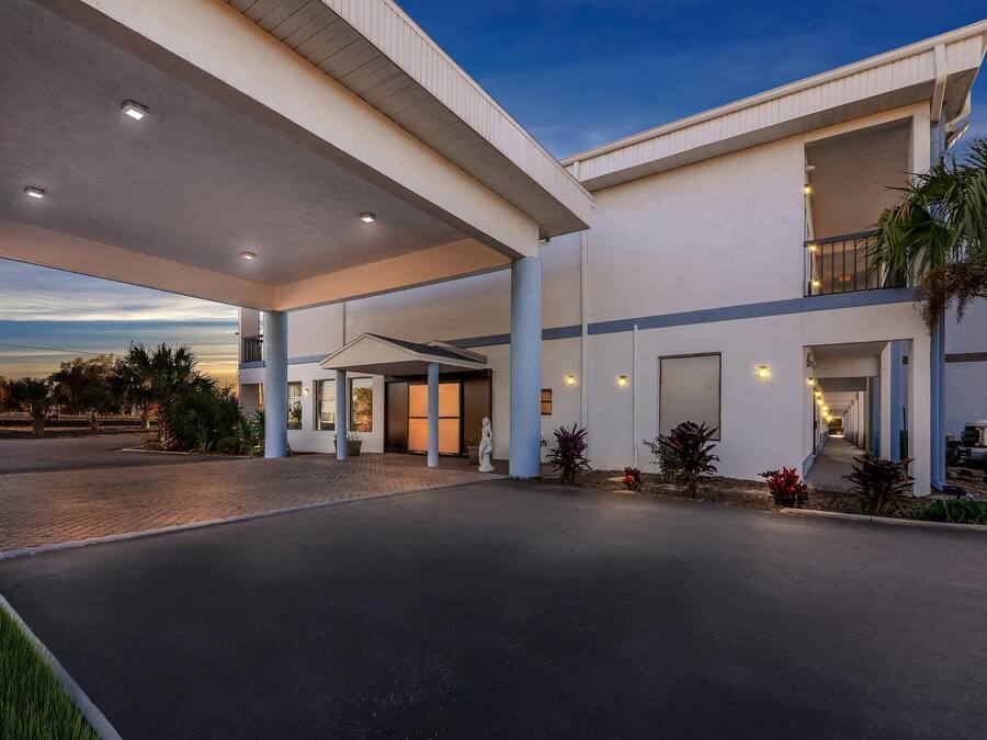 A modern hotel with a covered entrance, a second-floor balcony, and a landscaped driveway.