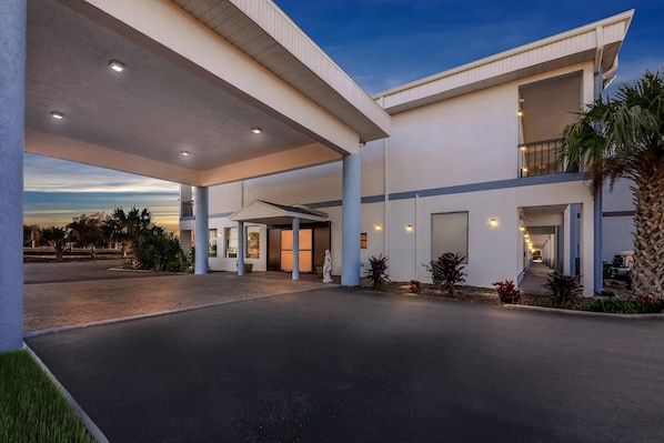 A modern hotel with a covered entrance, a second-floor balcony, and a landscaped driveway.