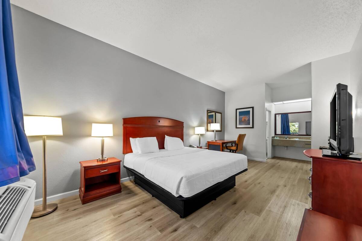 A hotel room with a large bed, bedside tables, a desk, and a television.
