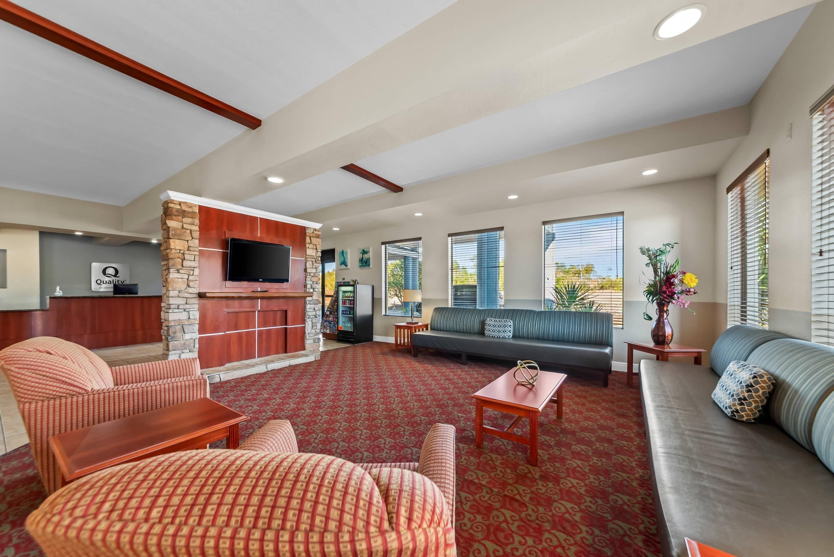 A spacious living area with a red patterned carpet, a stone fireplace, a flat-screen TV, a sofa, and a dining table.