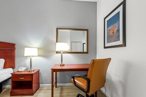 Habitación de hotel con cama, escritorio con lámpara, silla, mesita de noche con teléfono, espejo y un cuadro en la pared.