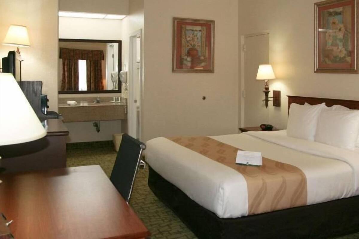 A hotel room with a bed, bedside tables, a desk, a mirror, and two wall-mounted lamps.