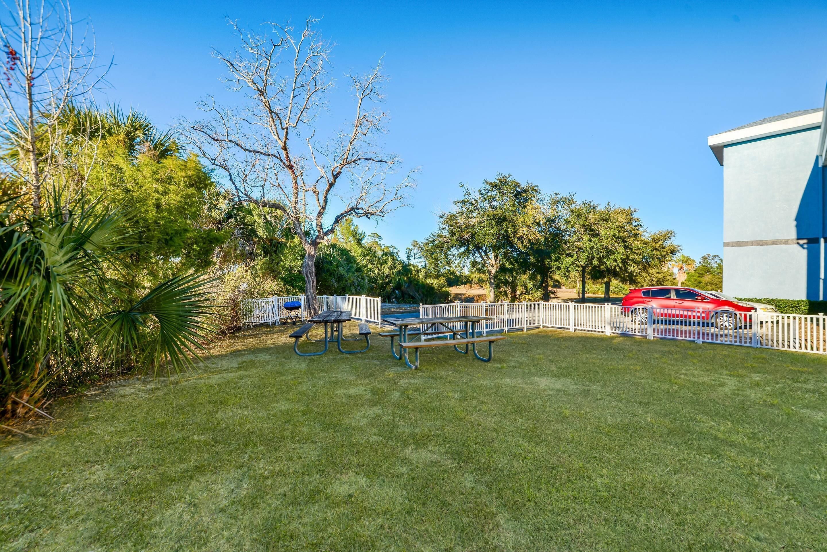 A well-maintained grassy area with picnic tables and a white fence.