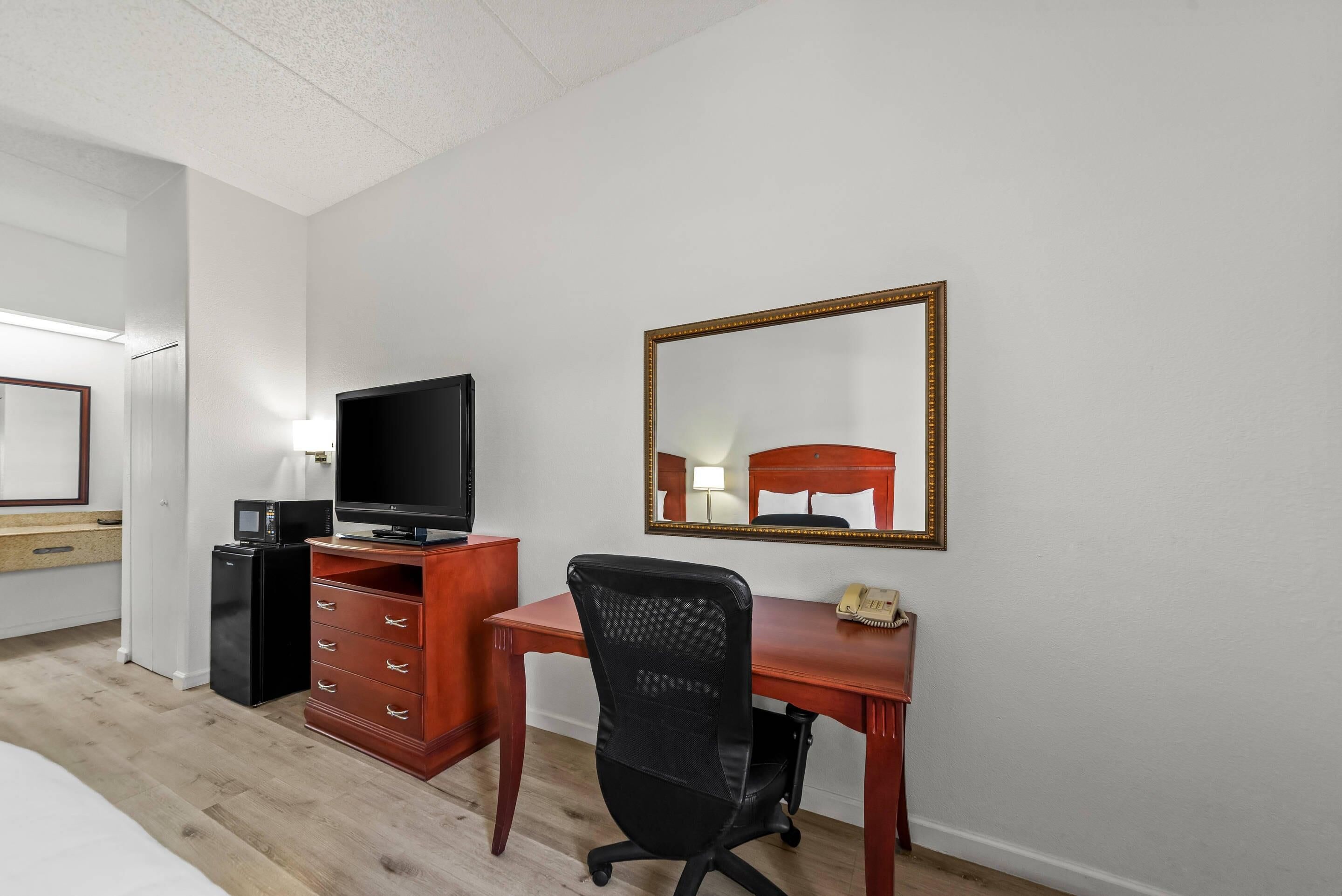 A hotel room with a wooden desk, a television, a mirror, and a telephone.
