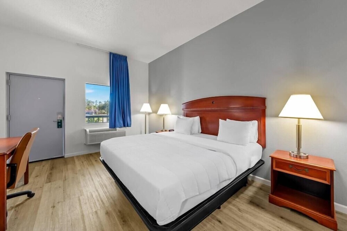 A hotel room with a bed, bedside lamps, a desk, and a window with curtains.