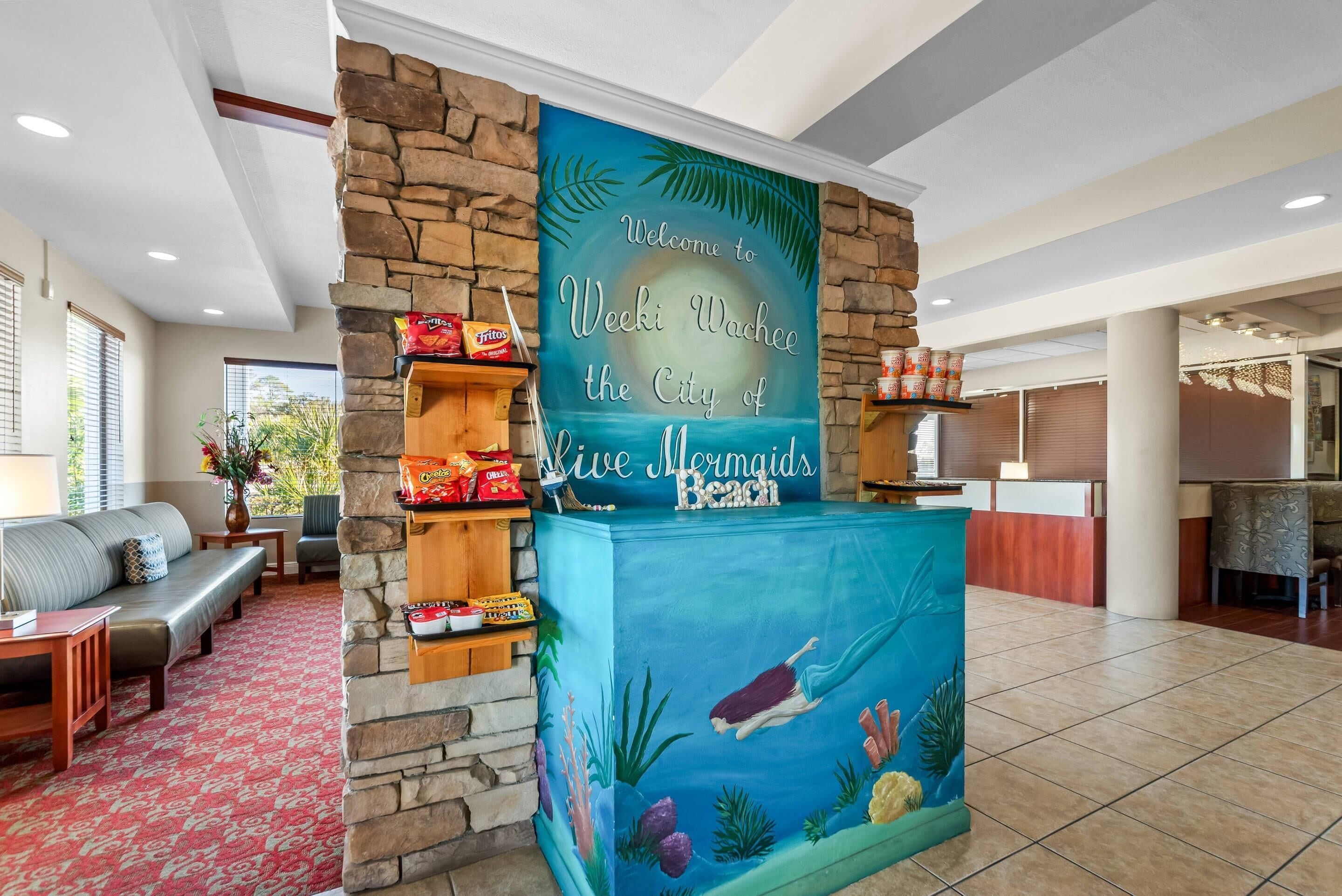 A reception area with a stone wall, a blue sign with a mermaid illustration, and a seating area with a sofa and chairs.