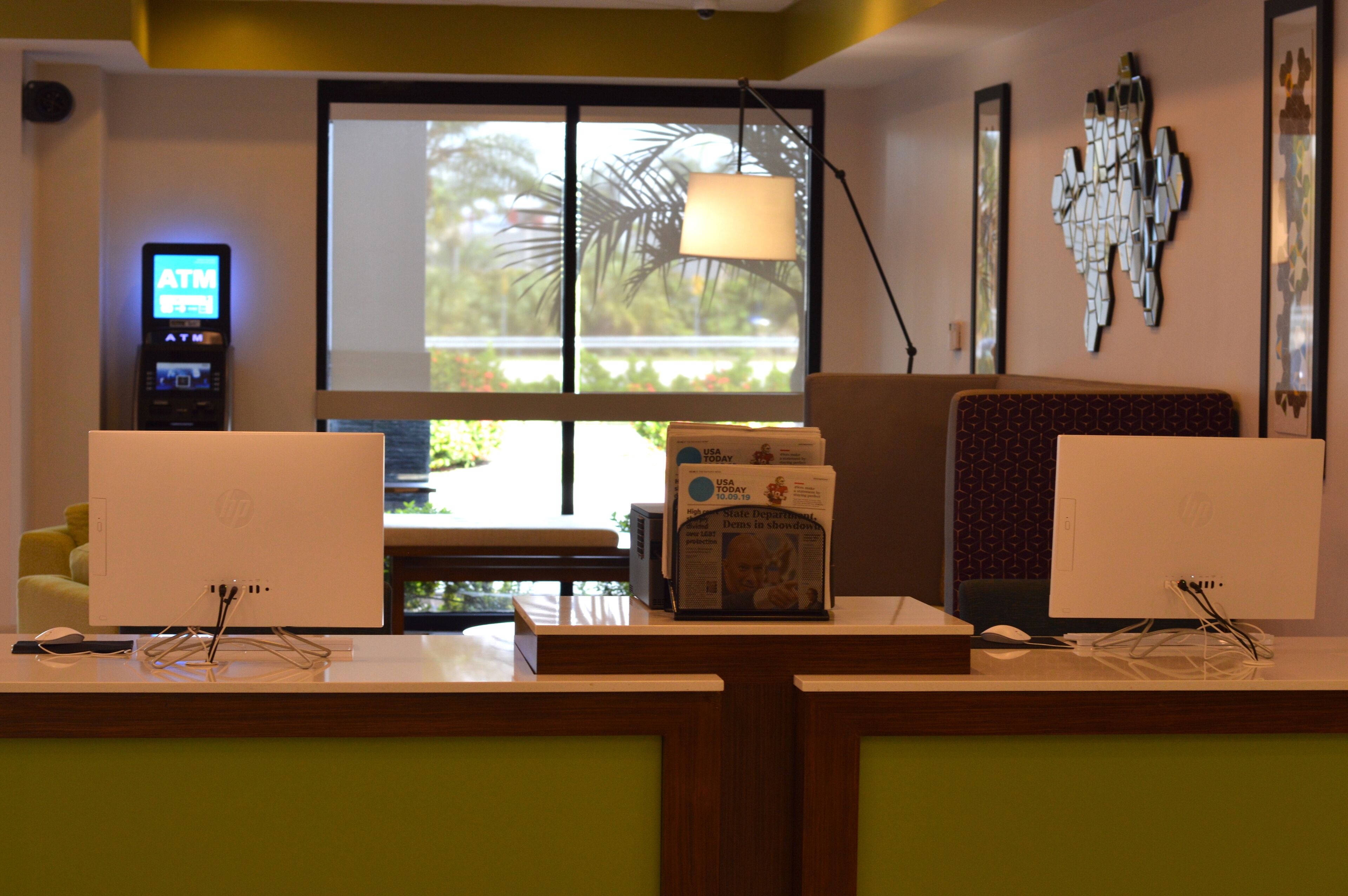Una mesa de recepción de hotel con dos monitores de computadora, un periódico y un cajero automático.