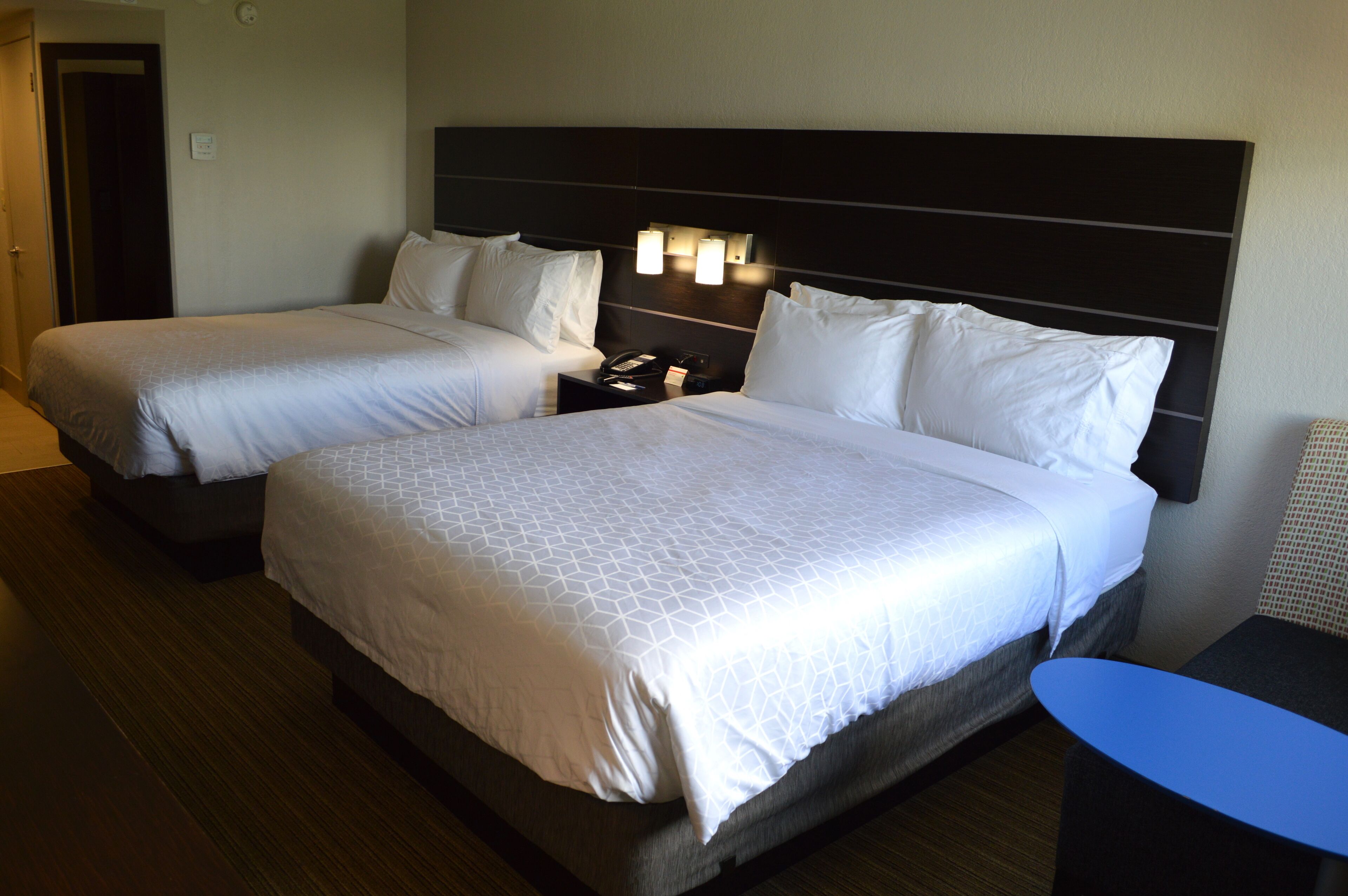 Una habitación de hotel con dos camas, una mesita de noche con un teléfono y una pequeña mesa azul.