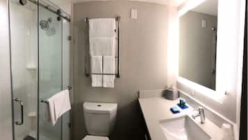 A bathroom with a glass shower enclosure, a toilet, a sink with a mirror, and a towel rack.