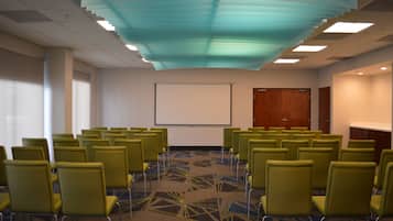 Une salle de conférence avec des rangées de chaises vertes, un écran de projection et une moquette à motifs.