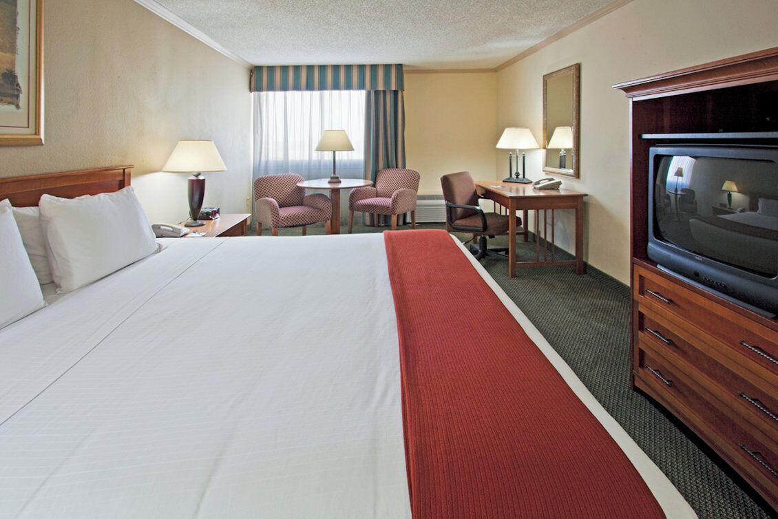 A hotel room with a large bed, a desk with a chair, a television, and a window with curtains.