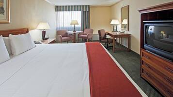 A hotel room with a large bed, a desk with a chair, a television, and a window with curtains.