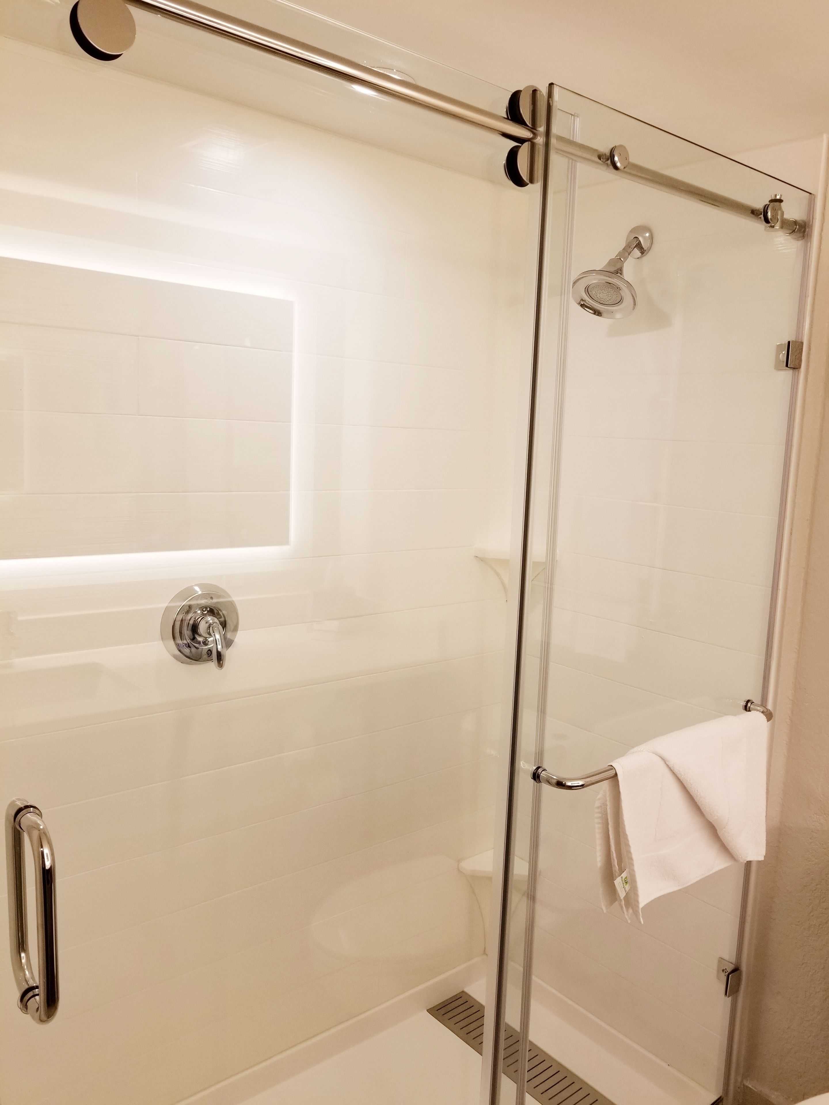Une douche fermée par des parois en verre, dotée d’un pommeau de douche à main, d’une porte en verre et d’une serviette accrochée à la poignée de la porte.
