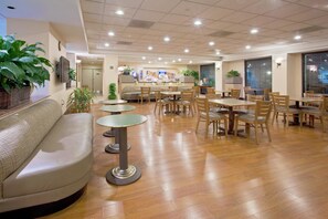 A spacious indoor dining area with wooden flooring, multiple tables and chairs, a sofa, and potted plants. - Holiday Inn Express & Suites Miami - Hialeah by IHG (Hialeah)