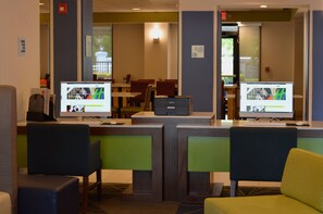 A reception area with two computer monitors displaying content, a reception desk, and a seating area with chairs. - Holiday Inn Express & Suites Miami - Hialeah by IHG (Hialeah)