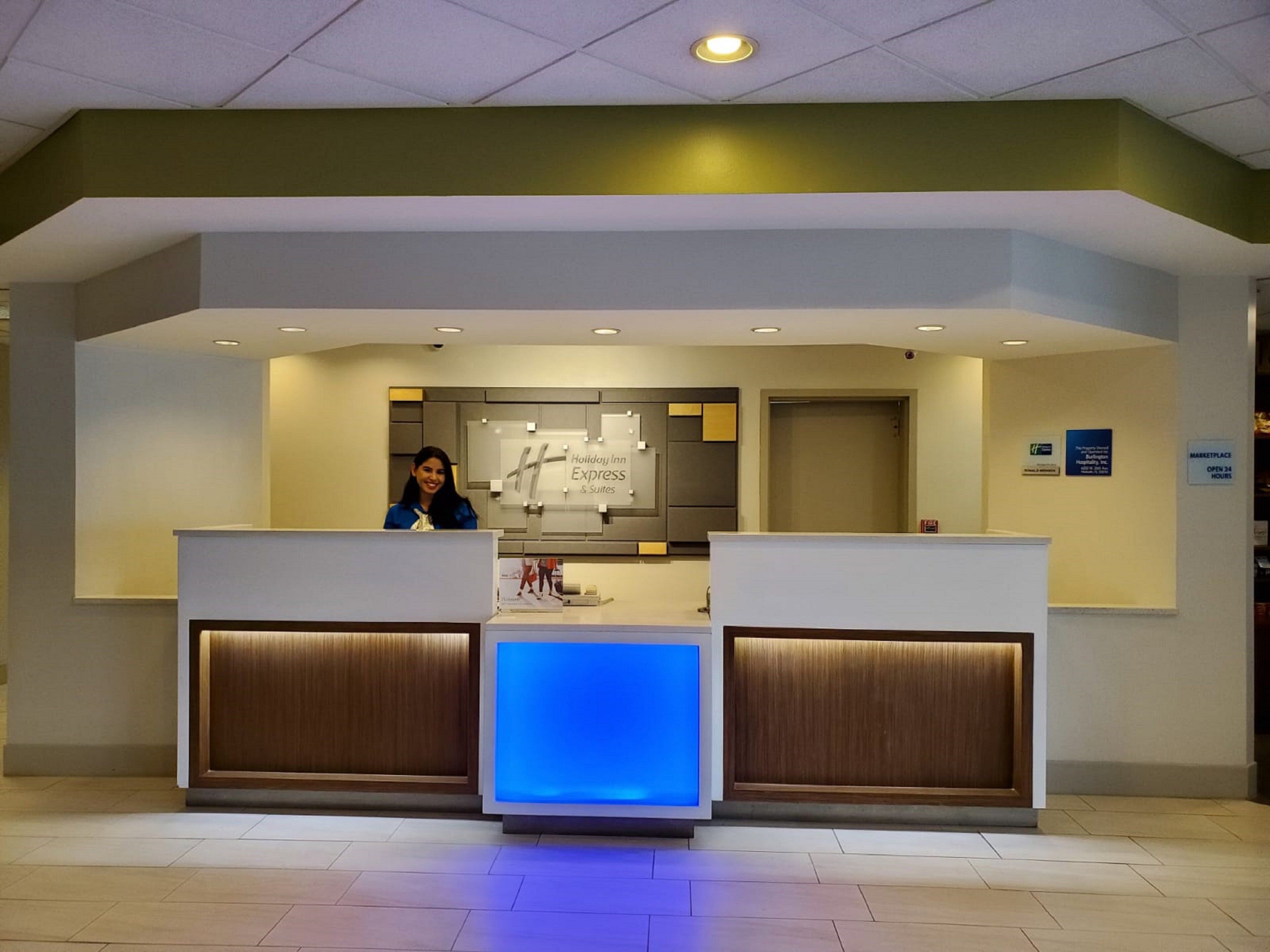 A reception desk with a digital display, a sign for Holiday Inn Express & Suites, and a Marketplace sign indicating 24-hour access.