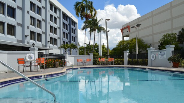 A swimming pool with a lifeguard tower, orange chairs, and a building with multiple windows in the background.