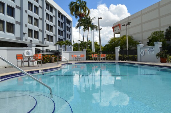 A swimming pool with a lifeguard tower, orange chairs, and a building with multiple windows in the background. - Holiday Inn Express & Suites Miami - Hialeah by IHG (Hialeah)
