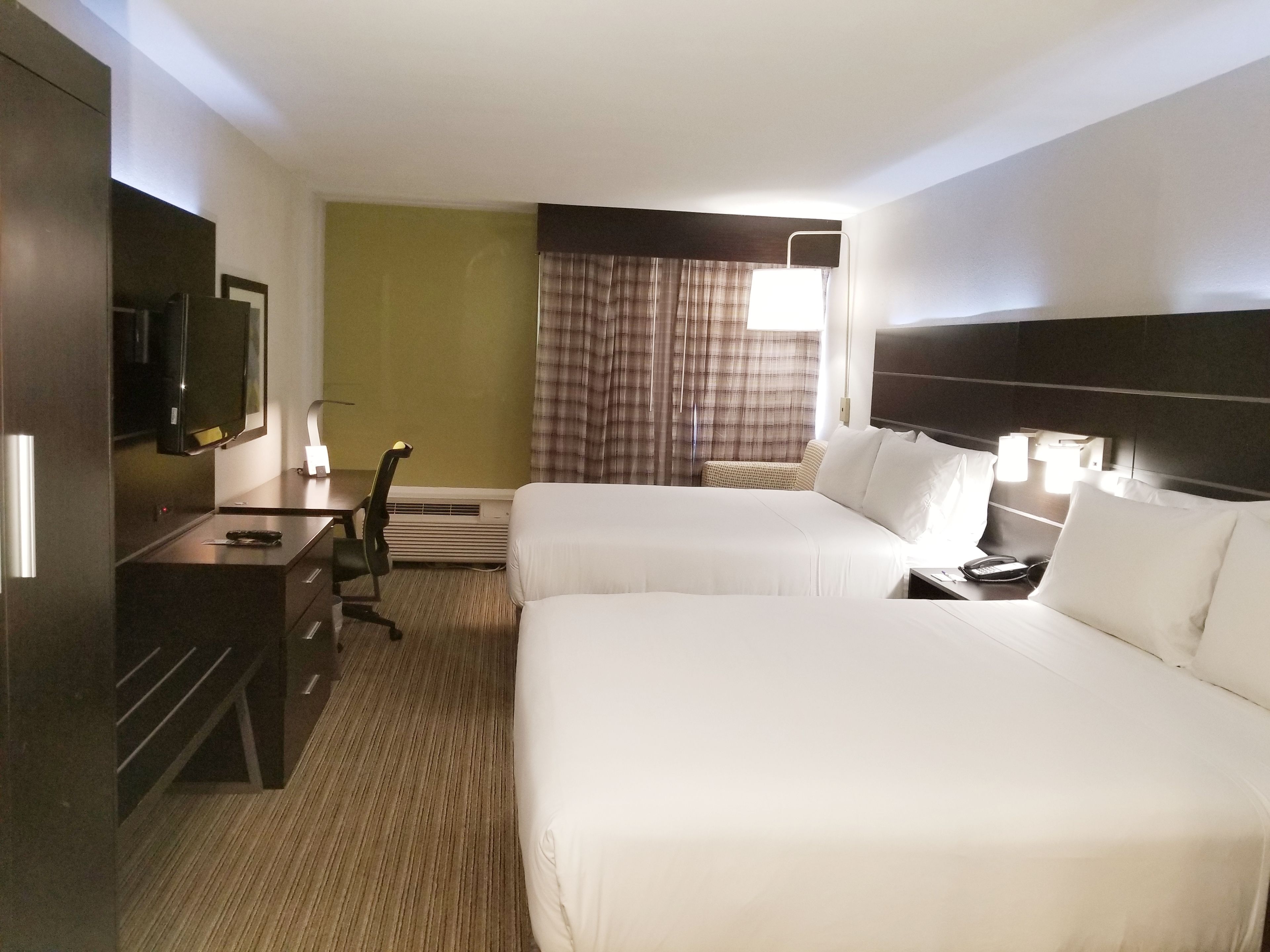 A hotel room with two beds, a desk with a chair, a television, and a window with curtains.