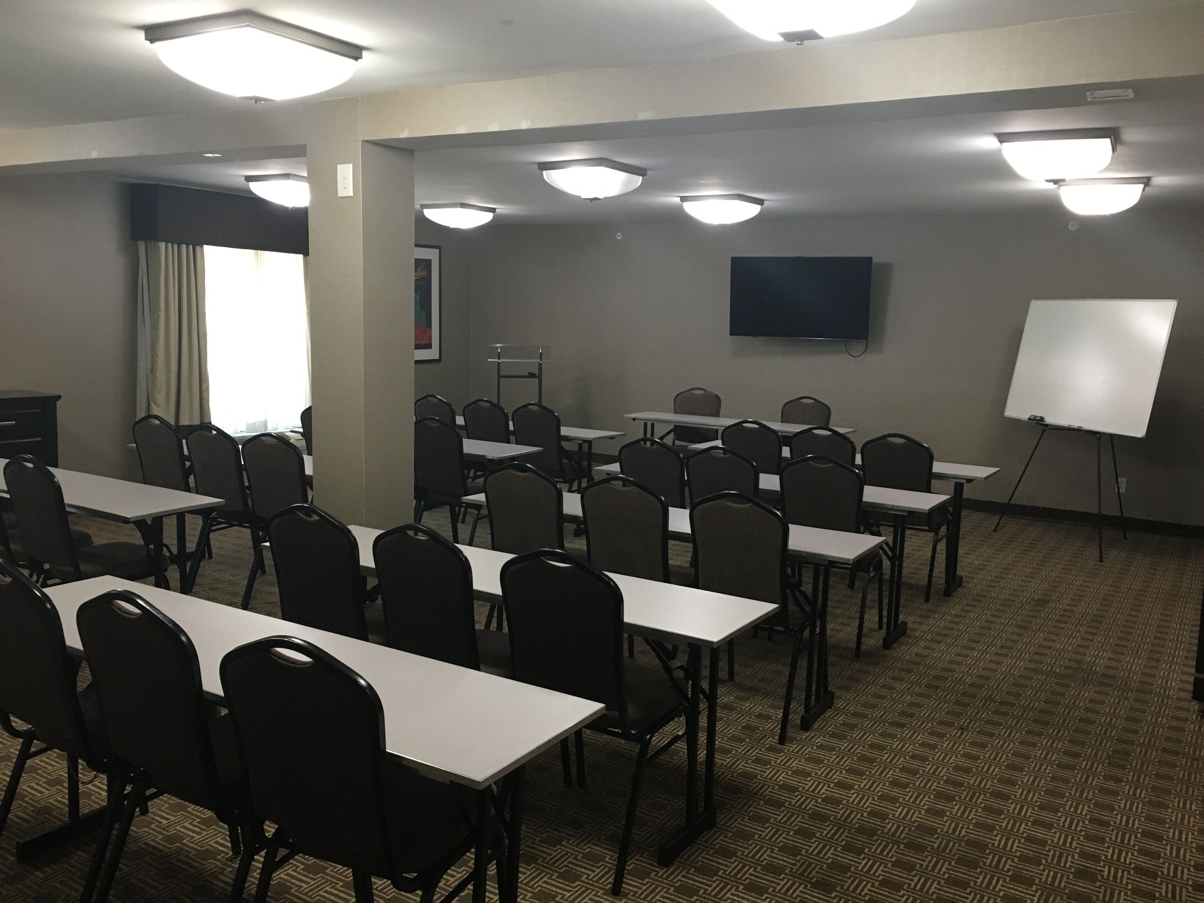 A conference room with multiple tables and chairs, a whiteboard, and a flat-screen TV on the wall.