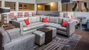 A modern living room with a sectional sofa, ottomans, a coffee table, and a floor lamp. - Quality Suites Nashville Airport (Nashville)