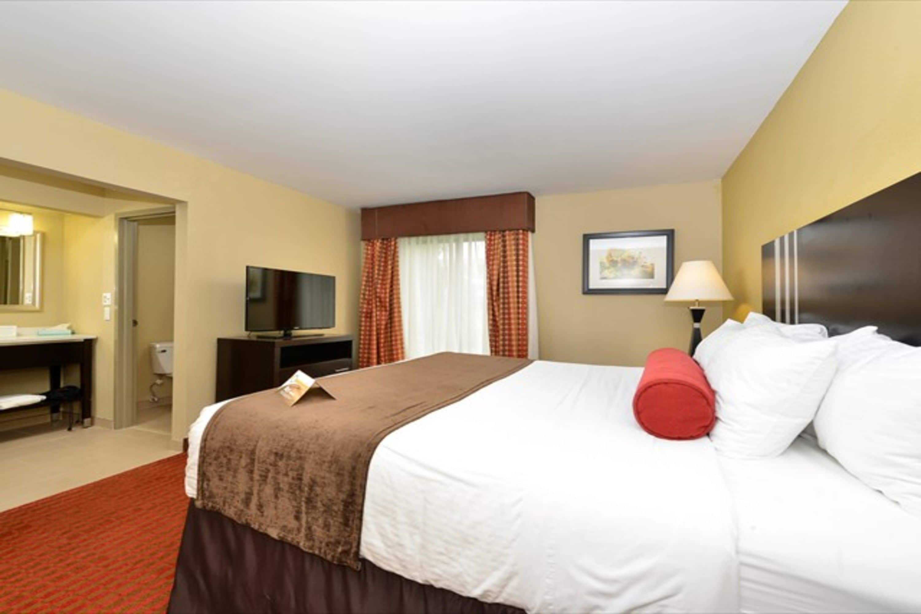 A hotel room with a bed, a desk, a television, and a window with curtains.
