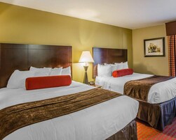 Una habitación de hotel con dos camas, una mesita de noche, una lámpara y un cuadro en la pared.