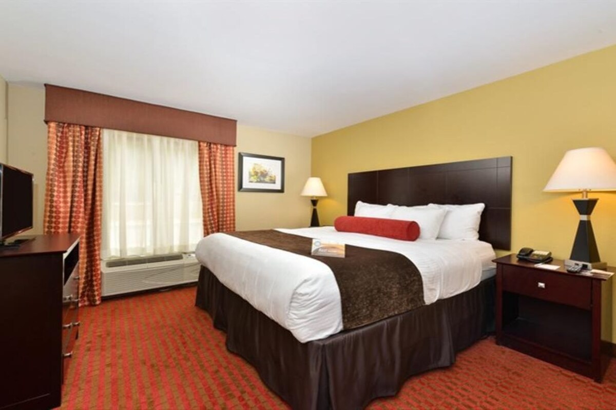 Habitación de hotel con una cama grande, dos mesitas de noche, un escritorio con silla, televisión y ventana con cortinas.