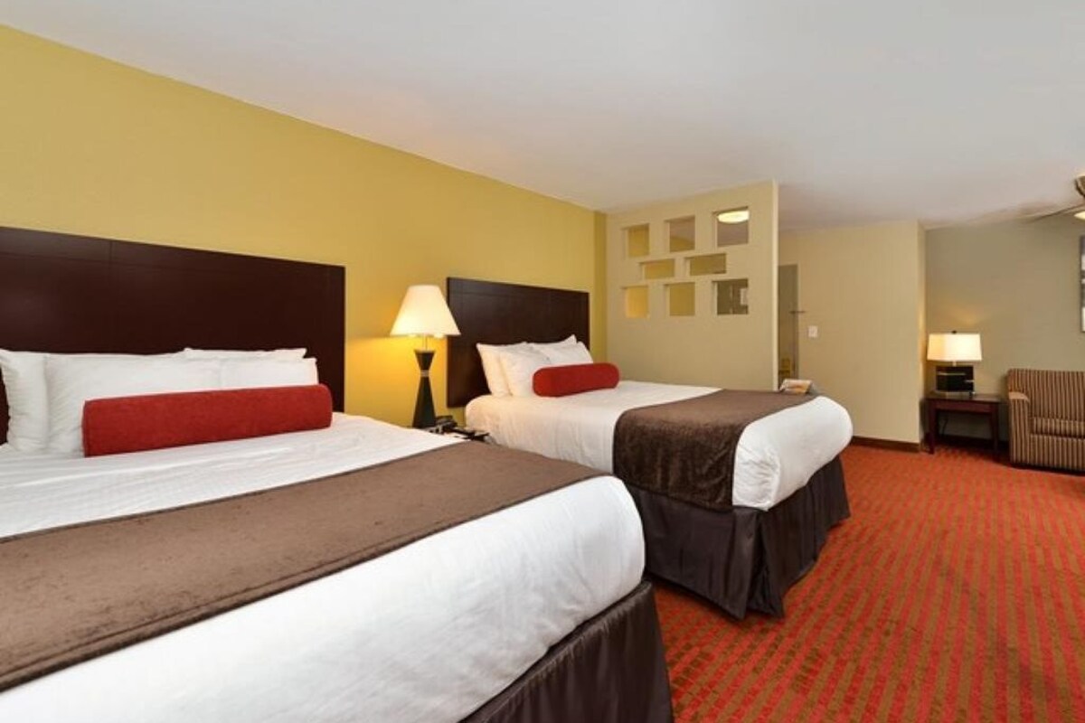 Habitación de hotel con dos camas, alfombra roja y una pequeña zona de estar.